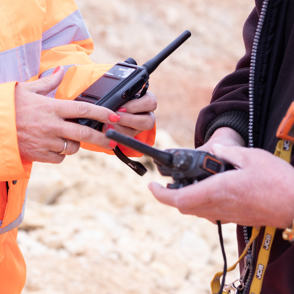two hands holding a two way radio on site